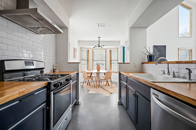 kitchen featuring a sink, appliances with stainless steel finishes, wall chimney range hood, and wood counters