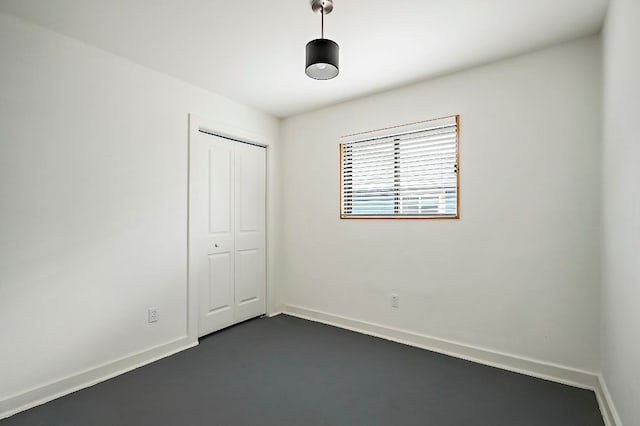 unfurnished bedroom featuring concrete flooring, a closet, and baseboards