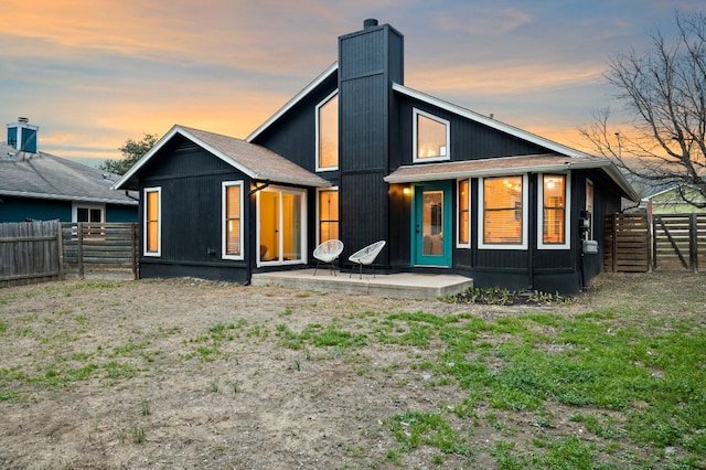 back of house at dusk featuring a patio area, a chimney, and a fenced backyard