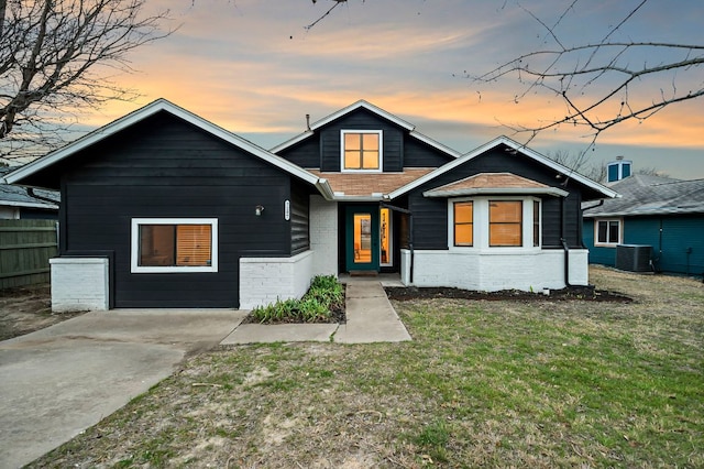 view of front of property with central air condition unit, brick siding, a shingled roof, fence, and a front yard