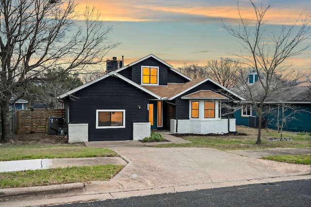 view of front of house featuring brick siding, a chimney, a shingled roof, concrete driveway, and fence