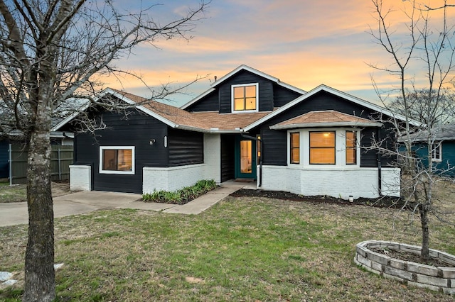 view of front of property with a front lawn, roof with shingles, fence, and brick siding