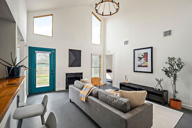 living room featuring finished concrete floors, visible vents, a fireplace, and a towering ceiling