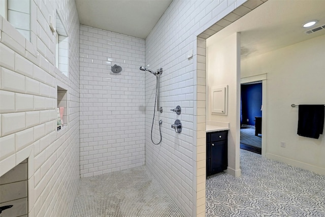 bathroom with visible vents, tiled shower, baseboards, and vanity