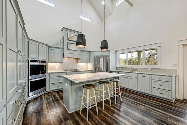 kitchen with a towering ceiling, dark wood-style floors, appliances with stainless steel finishes, a center island, and gray cabinets