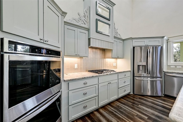 kitchen featuring light stone counters, dark wood finished floors, gray cabinetry, stainless steel appliances, and tasteful backsplash
