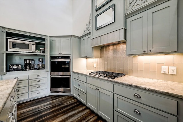 kitchen with gray cabinetry, light stone counters, decorative backsplash, stainless steel appliances, and dark wood-style flooring