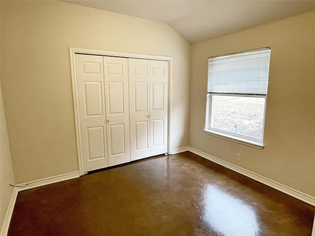 unfurnished bedroom featuring vaulted ceiling, concrete floors, a closet, and baseboards