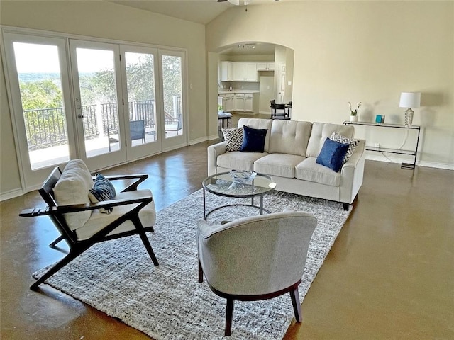 living area featuring arched walkways, lofted ceiling, and baseboards