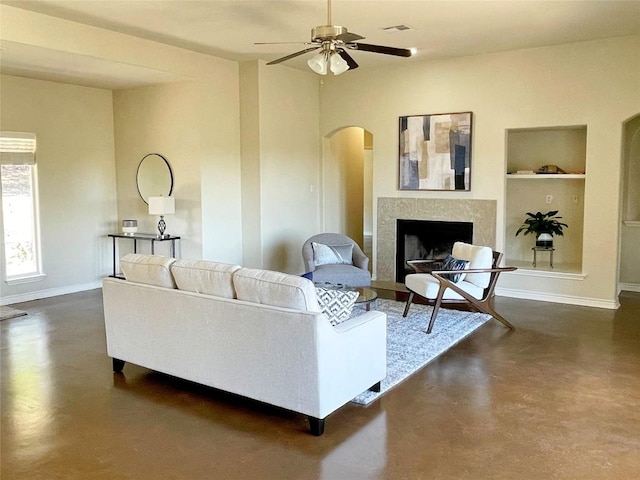 living room with arched walkways, visible vents, built in features, a tiled fireplace, and finished concrete floors