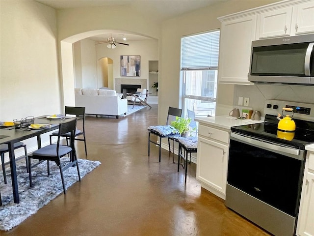 kitchen with concrete flooring, stainless steel appliances, arched walkways, and a ceiling fan