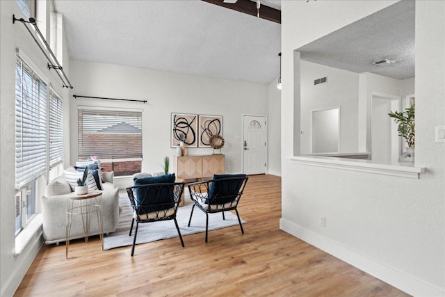 living area featuring visible vents, high vaulted ceiling, a textured ceiling, wood finished floors, and baseboards