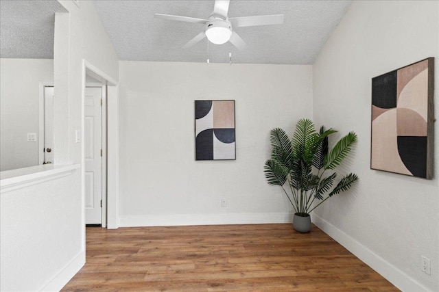 empty room with a textured ceiling, a ceiling fan, baseboards, and wood finished floors