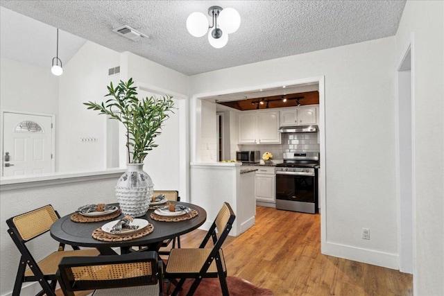 dining area featuring light wood finished floors, visible vents, a textured ceiling, and baseboards