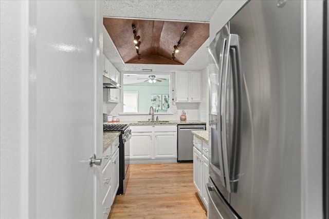 kitchen featuring a sink, under cabinet range hood, white cabinetry, appliances with stainless steel finishes, and light wood finished floors