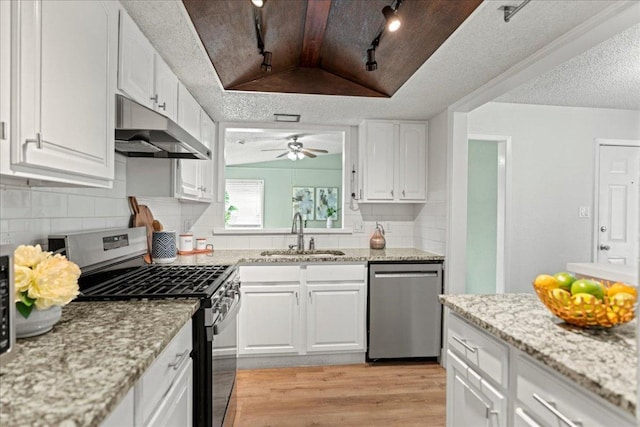 kitchen with under cabinet range hood, light wood-style flooring, stainless steel appliances, a textured ceiling, and a sink