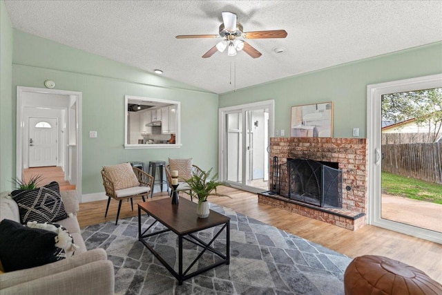 living area featuring a brick fireplace, lofted ceiling, wood finished floors, a textured ceiling, and a ceiling fan