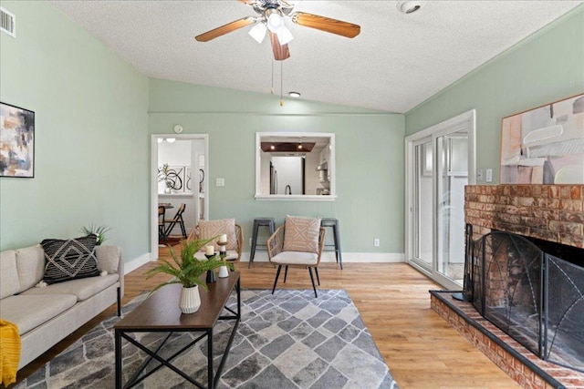 living area featuring a textured ceiling, wood finished floors, baseboards, a brick fireplace, and vaulted ceiling