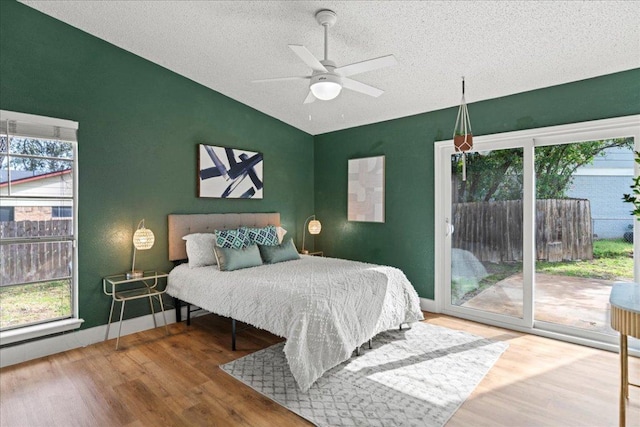 bedroom with a textured ceiling, wood finished floors, baseboards, access to exterior, and vaulted ceiling