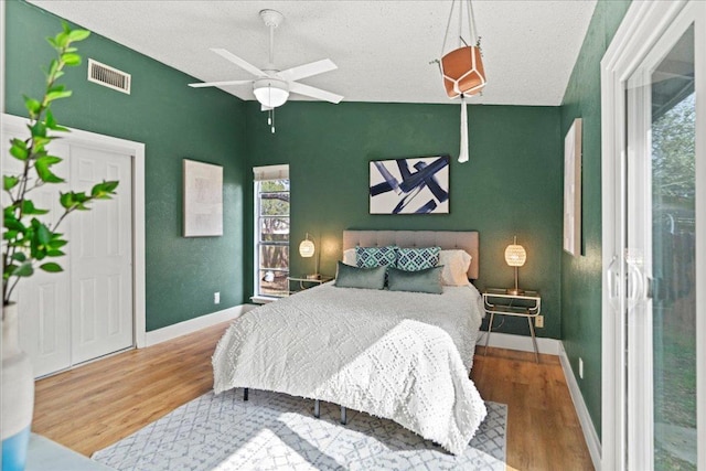 bedroom featuring visible vents, baseboards, lofted ceiling, wood finished floors, and a textured ceiling