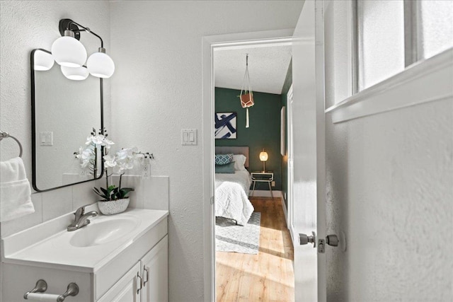 ensuite bathroom with vanity, wood finished floors, ensuite bath, decorative backsplash, and a textured wall