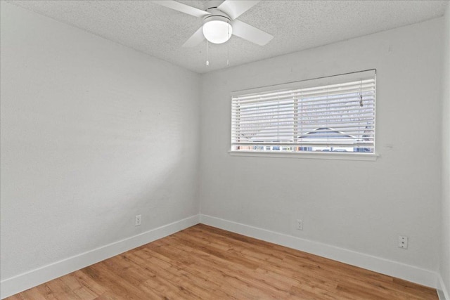 empty room with light wood-type flooring, baseboards, and a textured ceiling