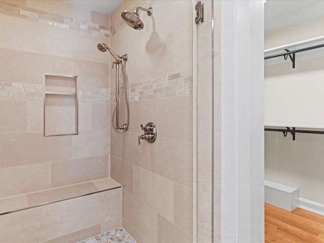 full bathroom featuring a spacious closet, a shower stall, and wood finished floors