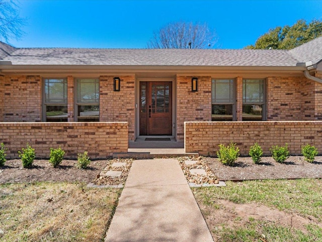 entrance to property featuring a porch, brick siding, and roof with shingles