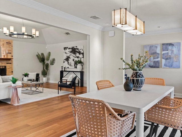 dining room with visible vents, wood finished floors, an inviting chandelier, crown molding, and a brick fireplace