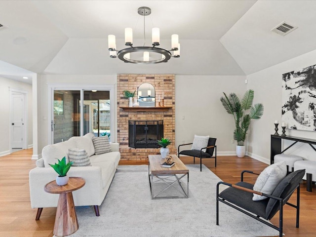 living area featuring visible vents, a chandelier, lofted ceiling, a fireplace, and wood finished floors