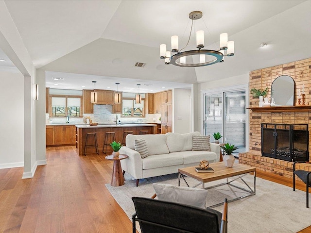 living area with visible vents, a notable chandelier, light wood finished floors, a brick fireplace, and vaulted ceiling