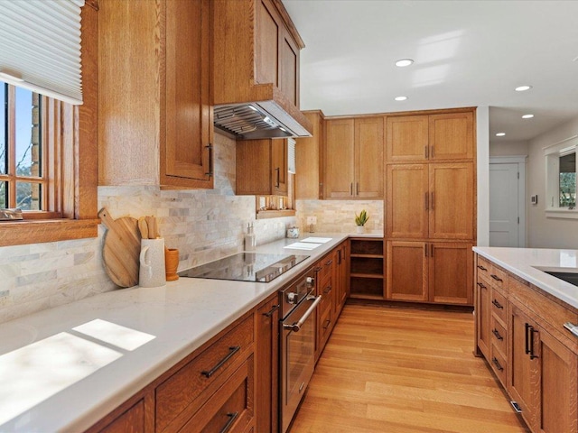 kitchen featuring light wood finished floors, light countertops, stainless steel oven, brown cabinets, and exhaust hood