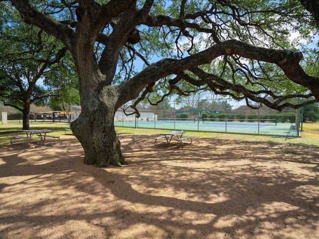 view of property's community featuring a tennis court and fence