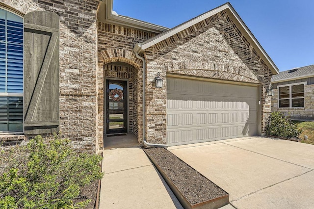 doorway to property with a garage, concrete driveway, and brick siding