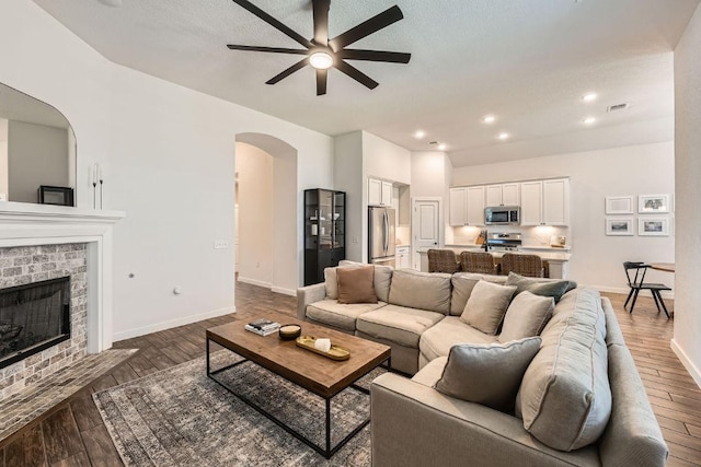 living area featuring baseboards, visible vents, arched walkways, dark wood-style floors, and a fireplace