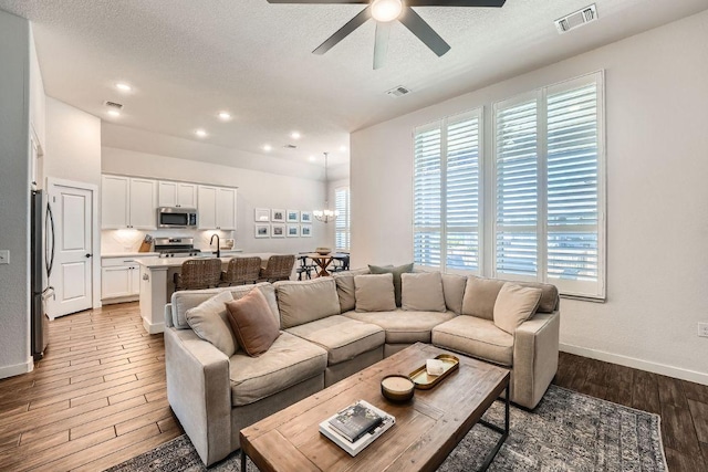 living room featuring light wood-type flooring, a textured ceiling, visible vents, and a ceiling fan