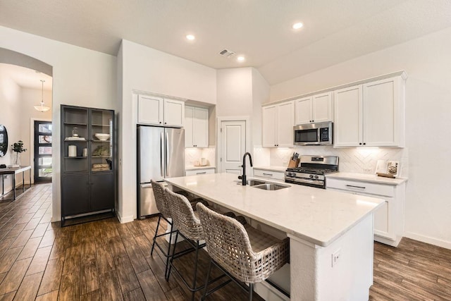 kitchen with arched walkways, stainless steel appliances, a sink, white cabinetry, and tasteful backsplash