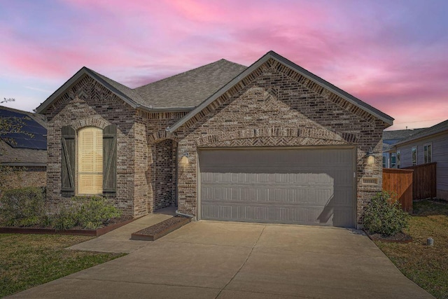 french provincial home with a garage, driveway, brick siding, and a shingled roof