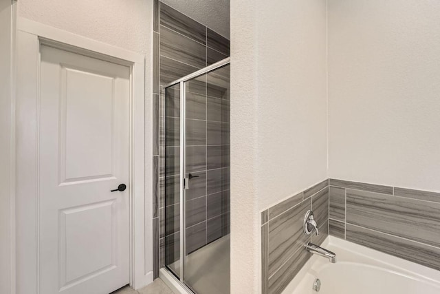 full bath with a textured ceiling, a textured wall, a stall shower, and a garden tub