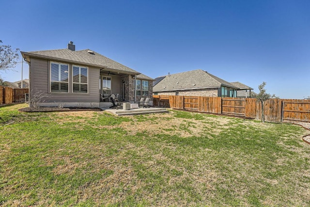 rear view of property with a patio area, a fenced backyard, a yard, and a chimney