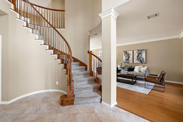 stairway featuring baseboards, ornamental molding, visible vents, and ornate columns