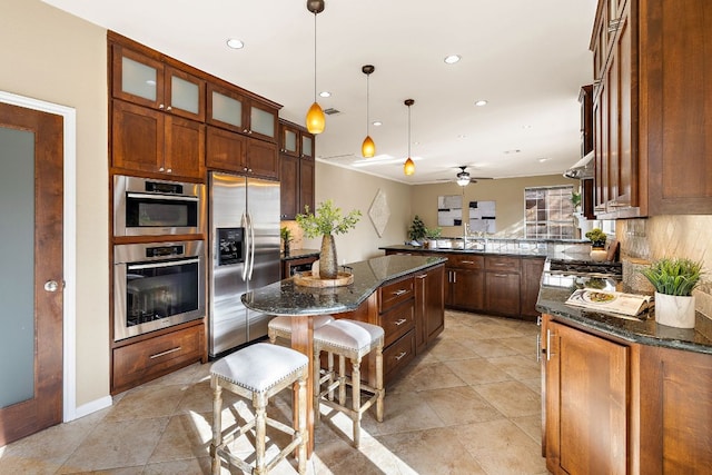 kitchen with a kitchen island, appliances with stainless steel finishes, decorative backsplash, dark stone counters, and glass insert cabinets