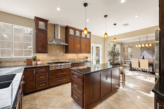 kitchen with stainless steel gas cooktop, tasteful backsplash, visible vents, hanging light fixtures, and wall chimney range hood