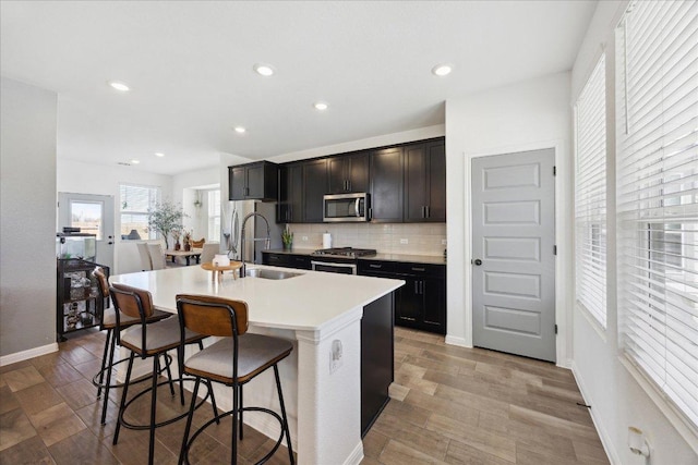 kitchen featuring a kitchen island with sink, a sink, stainless steel appliances, a breakfast bar area, and decorative backsplash
