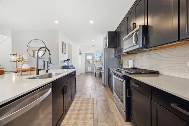 kitchen featuring light wood-type flooring, a sink, tasteful backsplash, appliances with stainless steel finishes, and light countertops