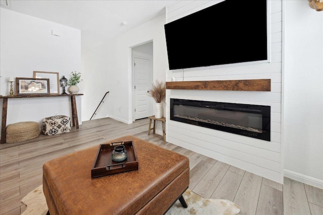living area with baseboards, a large fireplace, and wood finished floors