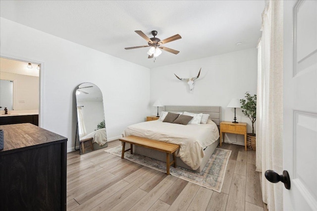 bedroom featuring baseboards, arched walkways, ceiling fan, a sink, and light wood-style floors