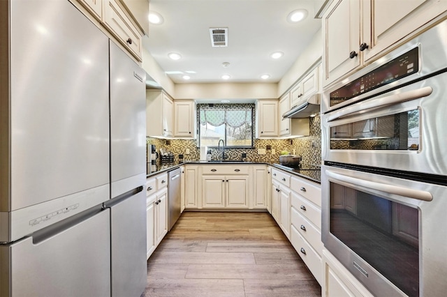 kitchen featuring visible vents, light wood-style flooring, a sink, appliances with stainless steel finishes, and dark countertops