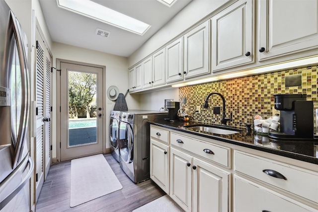 laundry area with visible vents, washer and clothes dryer, wood finished floors, cabinet space, and a sink