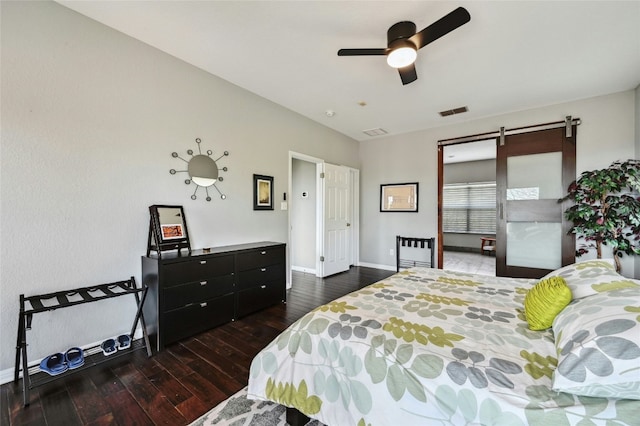 bedroom with visible vents, a barn door, dark wood-type flooring, ceiling fan, and baseboards